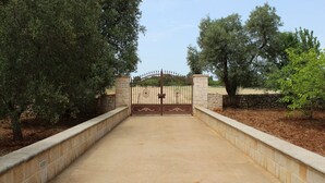 Una entrada protegida con muro de piedra y reja de metal, rodeada de árboles.