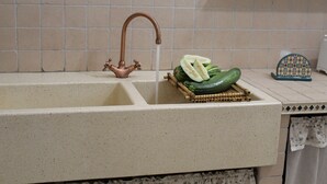 Un lavamanos de cocina con grifo de cobre, una cesta tejida con vegetales cortados y una bandeja estampada.