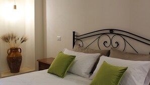 Una cama bien hecha con almohadas blancas y verdes, un jarrón marrón con plantas secas y una mesita de noche de madera.