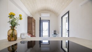 A hallway with a reflective floor, a wooden cabinet, a white vase with yellow flowers, and a door leading to a bright outdoor area.