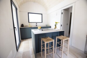 A modern kitchen with a central island, two bar stools, and a large window.