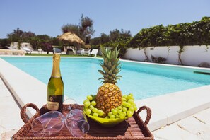 A poolside setting with a bottle of wine, a pineapple, and grapes on a tray. - borgo della mimosa (San Vito dei Normanni)