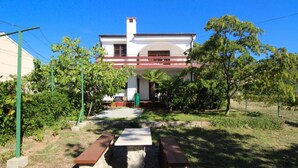 A house with a patio area, two benches, and a small garden with trees and shrubs. -   apartment Hope with AC and  WiFi (Punat)