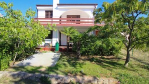 A two-story building with a central archway, surrounded by lush greenery and a stone pathway leading to the entrance. -   apartment Hope with AC and  WiFi (Punat)
