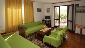 A living room with a green sofa, a coffee table, and a TV. There is a sliding glass door leading to an outdoor area. -   apartment Hope with AC and  WiFi (Punat)
