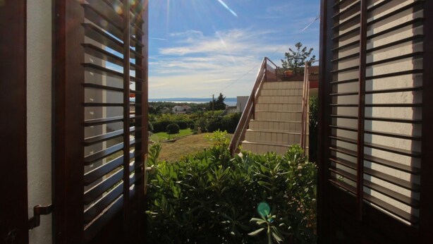 A view through open shutters to a garden with a clear sky and distant landscape. -   apartment Hope with AC and  WiFi (Punat)