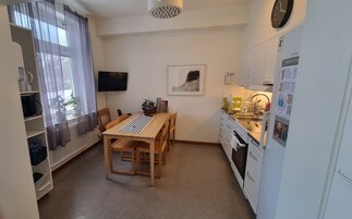 Ett kompakt kök med ett matbord, stolar, ett kylskåp och en diskho.