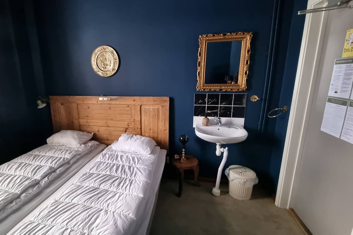 A bedroom with a wooden headboard, two beds with white bedding, a white sink, a mirror, and a trash bin.