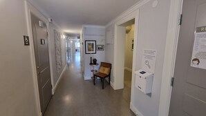 A hotel hallway with a chair, a small table with a plant, and a key box on the wall.