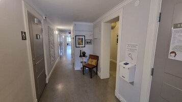 En hotellkorridor med en stol, ett litet bord med en växt och en nyckelbox på väggen.