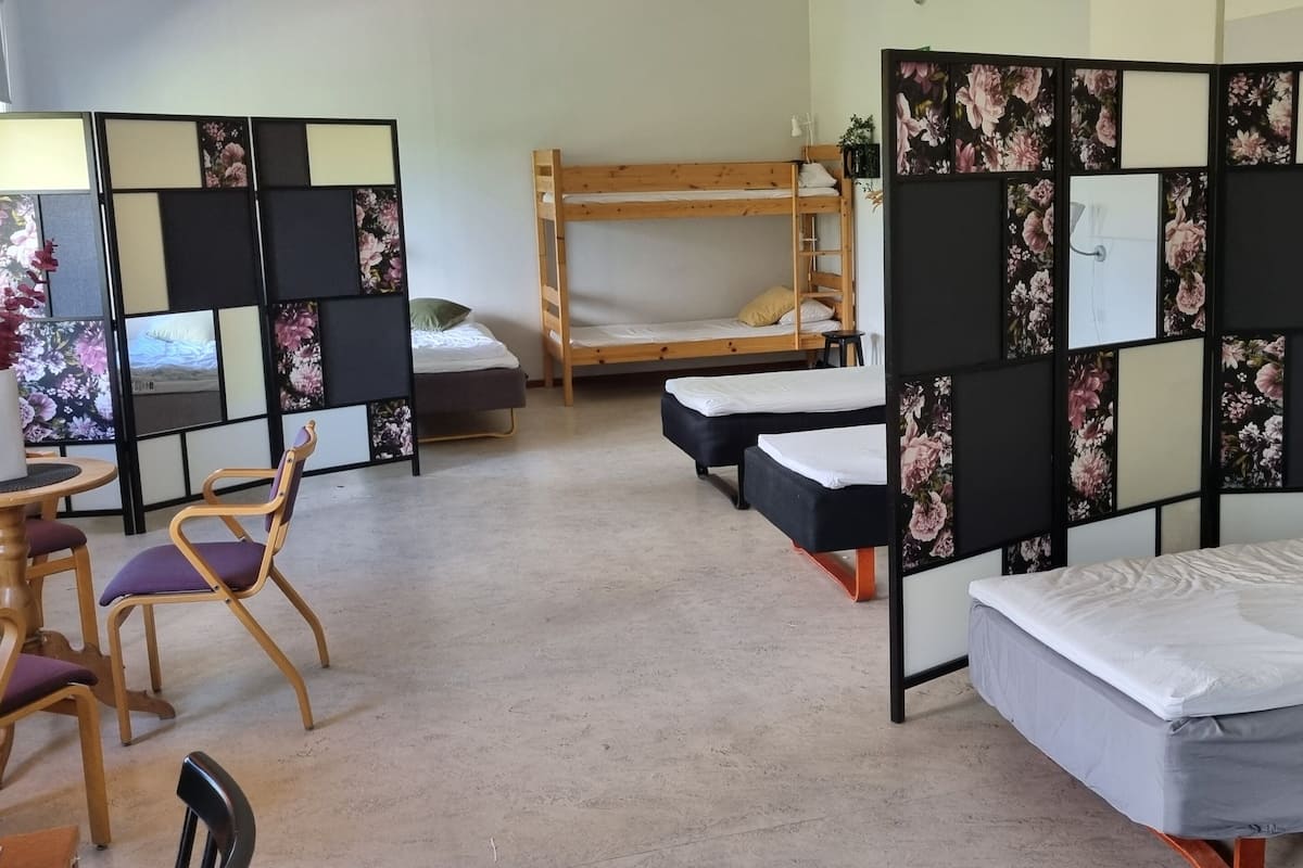A dormitory room with bunk beds, a desk, chairs, and a partition with floral panels.