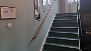 A staircase with a handrail, a wall-mounted sign with room labels, and a modern light fixture.