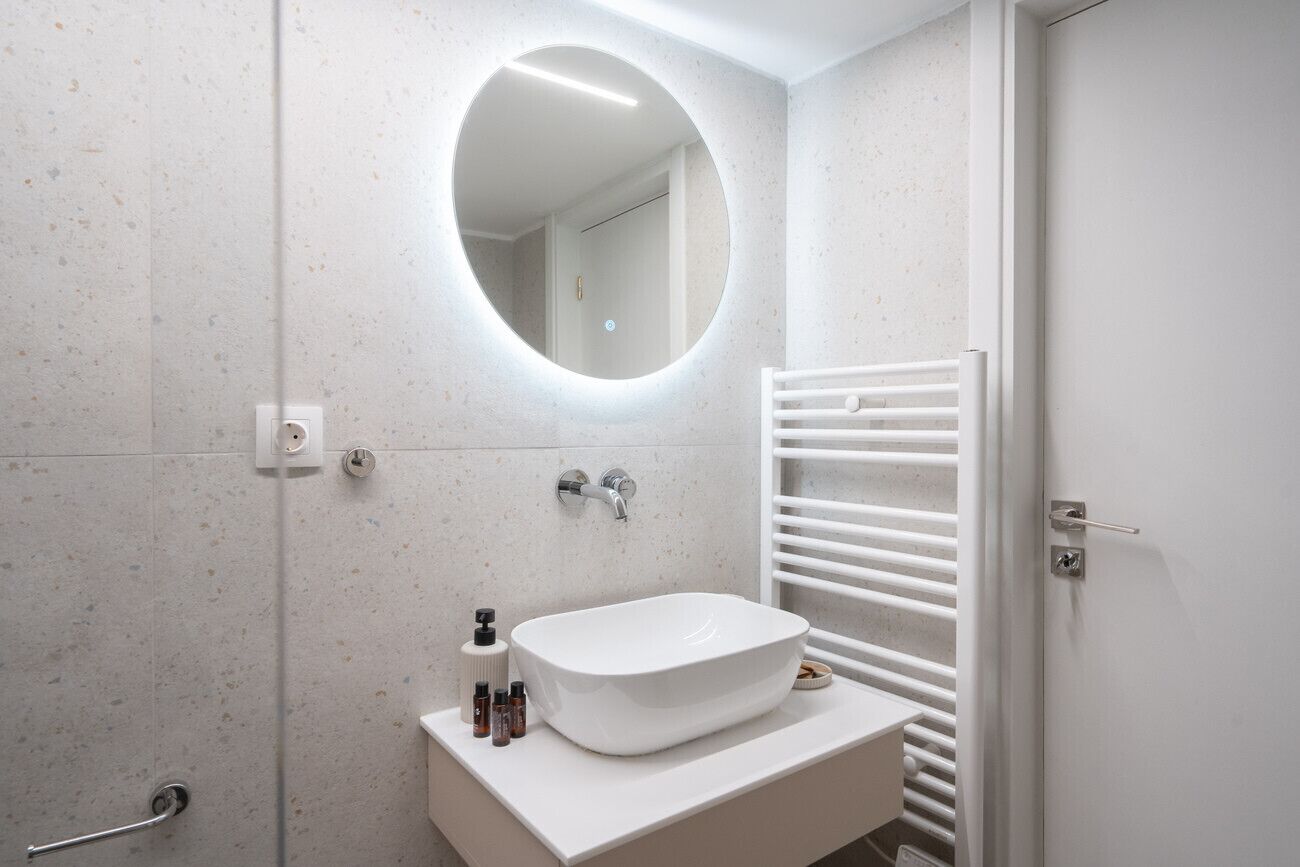 Een moderne badkamer met een vrijstaand badmeubel, een ronde spiegel, een handdoekhouder en een deur.