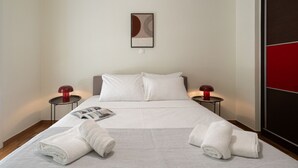 Una cama bien hecha con sábanas blancas, dos mesitas de noche con lámparas rojas y una obra de arte abstracta enmarcada en la pared.
