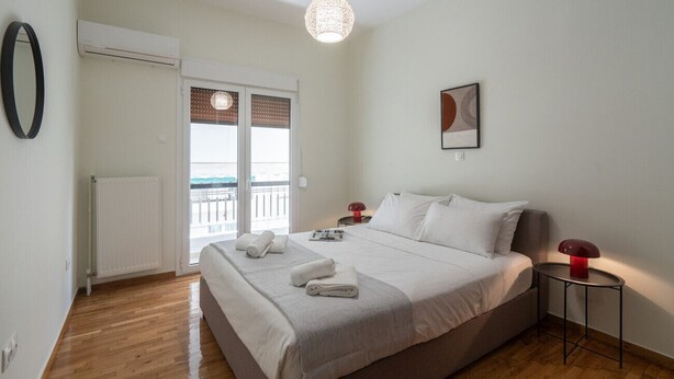 Una habitación de hotel con cama, mesita de noche, lámpara, radiador y ventana con persianas, con vistas al exterior.
