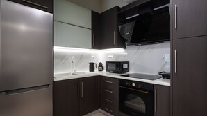 Una cocina moderna con armarios oscuros, un refrigerador de acero inoxidable, un microondas, una cafetera y un horno empotrado.