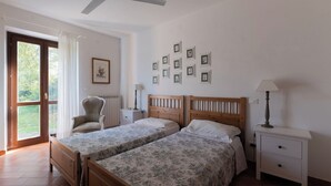 Une chambre avec deux lits, une chaise, une table de chevet, une lampe et un ventilateur de plafond.