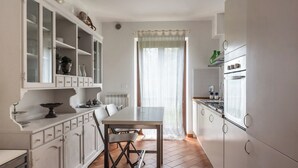 Une cuisine avec des meubles blancs, une table à manger et une fenêtre ornée de rideaux légers.