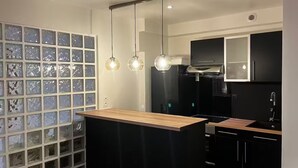 Moderni keittiö, jossa on keskeinen saareke, mustat kaapit ja lasimosaiikkilaatoilla päällystetty välitila.