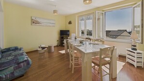 A dining area with a table and chairs, a television, and a window with a view of buildings. - The port and beaches nearby - 2 adults 2 children (Concarneau)