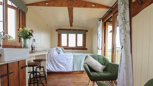 Une pièce confortable avec un lit, un fauteuil vert, un bureau en bois avec une chaise et une fenêtre avec des rideaux.