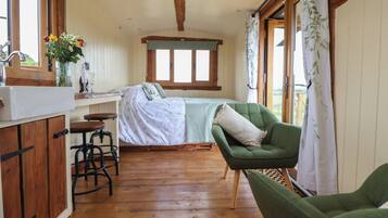 A cozy room with a bed, a green armchair, a wooden desk with a chair, and a window with curtains.