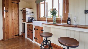 Une cuisine avec des meubles de rangement en bois, une machine à café, un évier et deux tabourets.