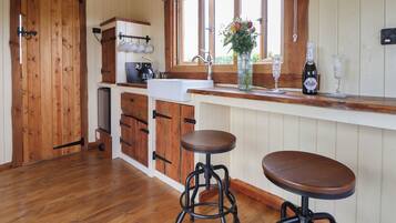 A kitchen with wooden cabinets, a coffee machine, a sink, and two stools.