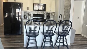 A modern kitchen with a central island, black chairs, and a refrigerator. - Book Fast! 2BR/2BA Ocean Block—Steps to Beach, Walk to Top Restaurants &! (Ocean City)