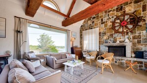 Un salon chaleureux avec une cheminée en pierre, des poutres apparentes et des fauteuils confortables.