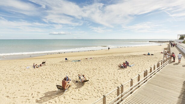 Une vaste plage de sable, avec une promenade en bois, un ciel dégagé et une mer calme.