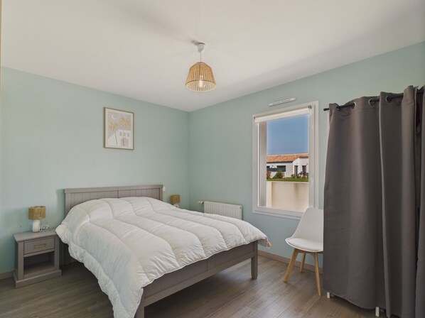A bedroom with a bed, bedside tables, a chair, a window with curtains, and a hanging light fixture.