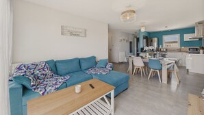 Un salon moderne avec un canapé bleu, une table basse en bois et un coin repas comprenant une table et des chaises blanches.