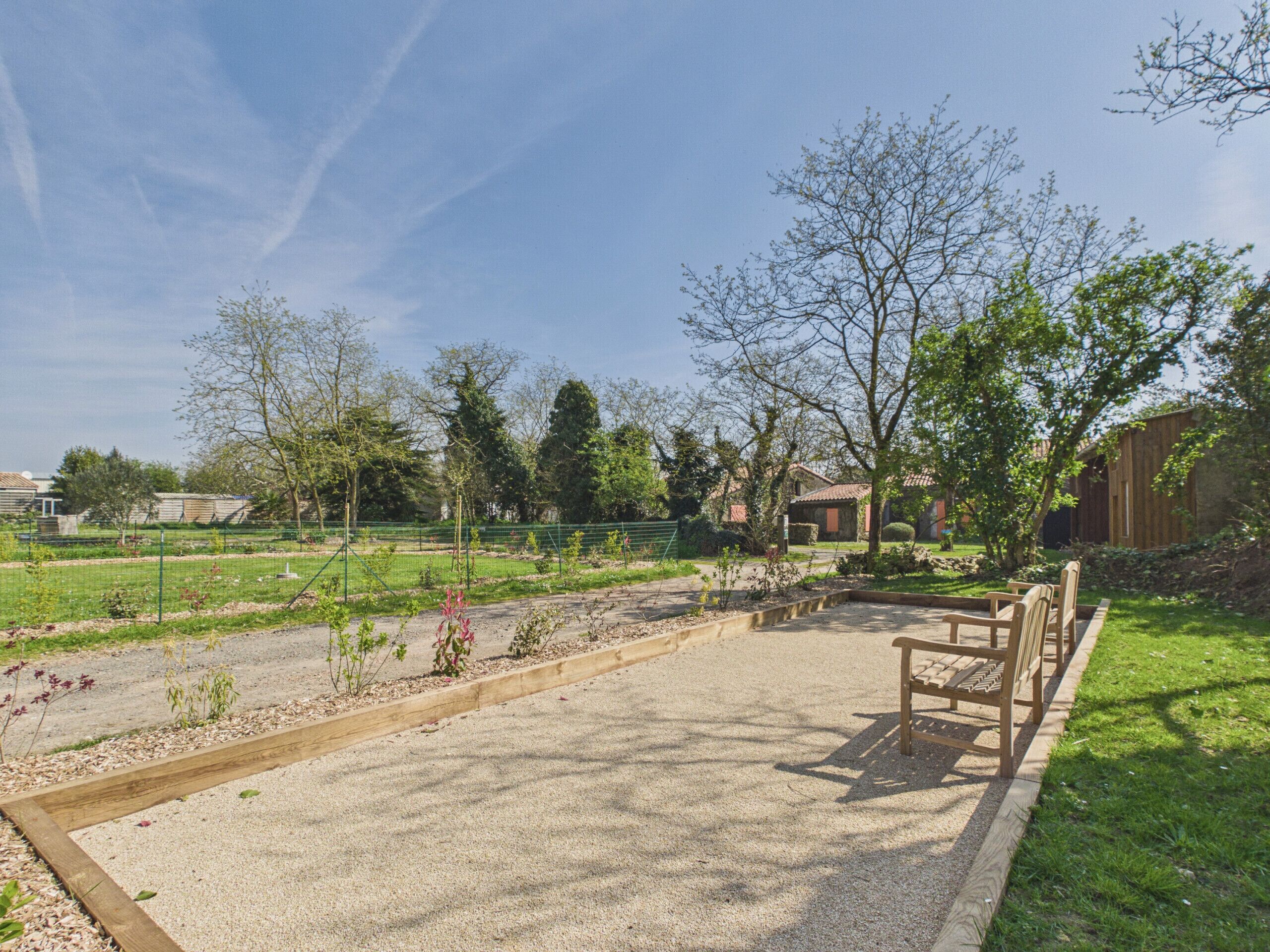 A park with a gravel area, wooden benches, and a green fence.