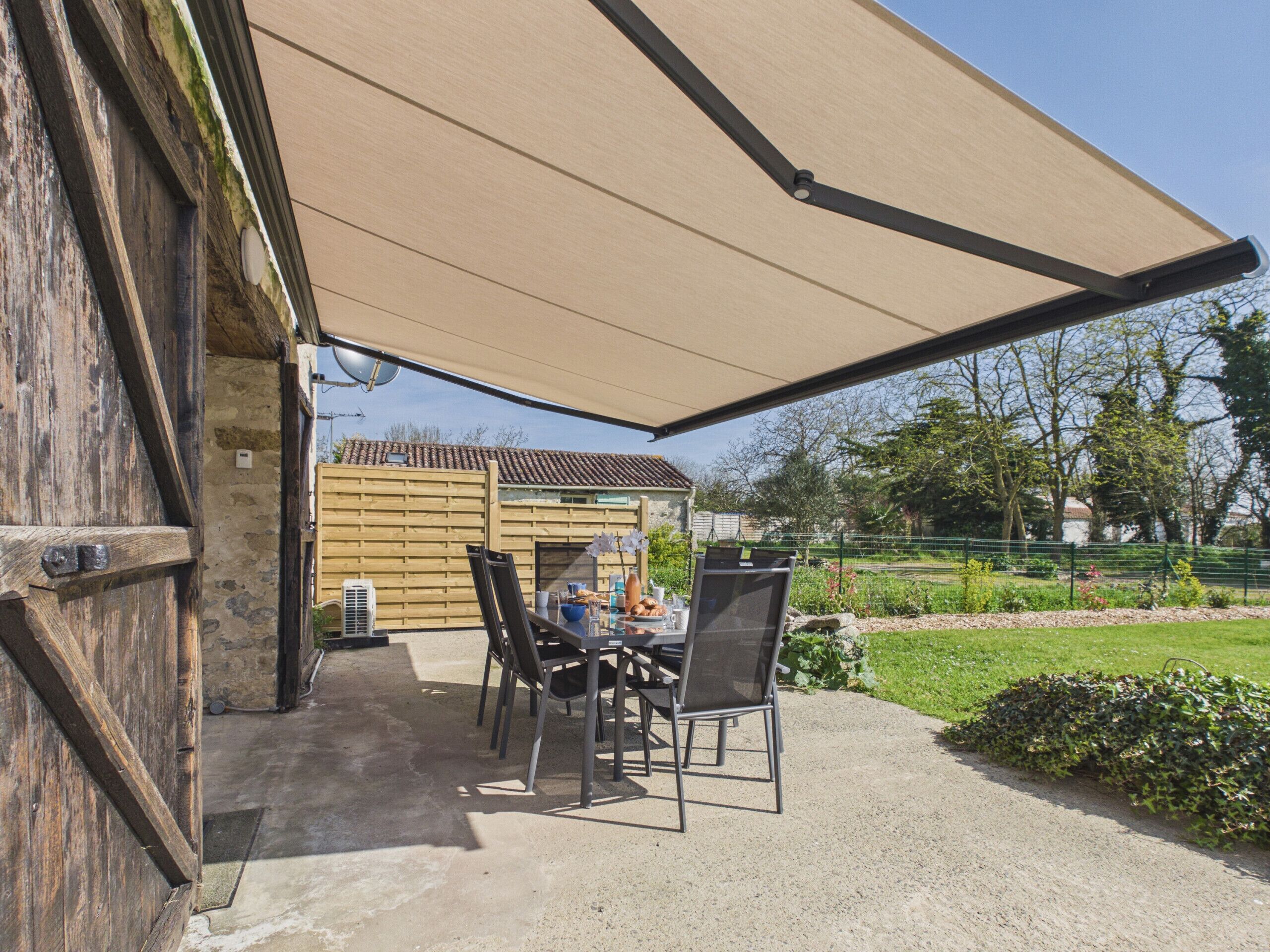 Une terrasse extérieure avec une table et des chaises, un grand parasol et un mur en pierre.