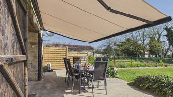Une terrasse extérieure avec une table et des chaises, un grand parasol et un mur en pierre.