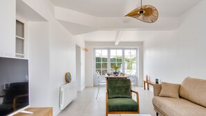 A modern living room with a TV, a green armchair, a beige sofa, and a dining area with a table and chairs. - 200m from the beach-House at Vieil-For 4-Garden (Noirmoutier-en-l´Ile)