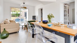 A modern living room with a sofa, clear chairs, a wooden dining table, and a kitchen area with a fridge and cabinets. - 200m from the beach-House at Vieil-For 4-Garden (Noirmoutier-en-l´Ile)