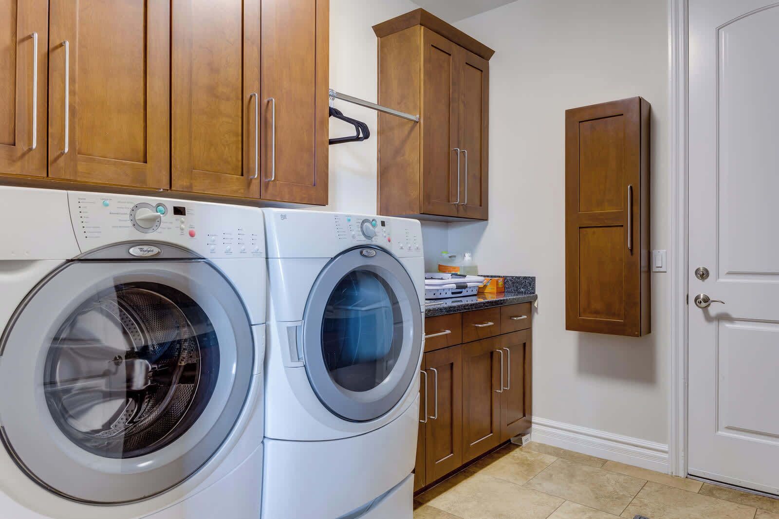 A laundry area with two front-loading washing machines, wooden cabinets, and a white door.