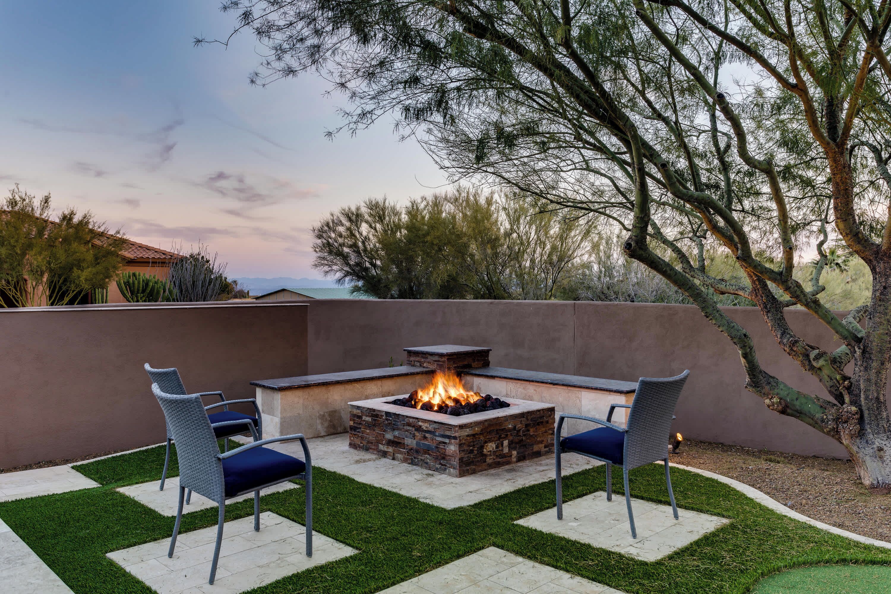 An outdoor patio with a stone fire pit, two chairs, and a small table.