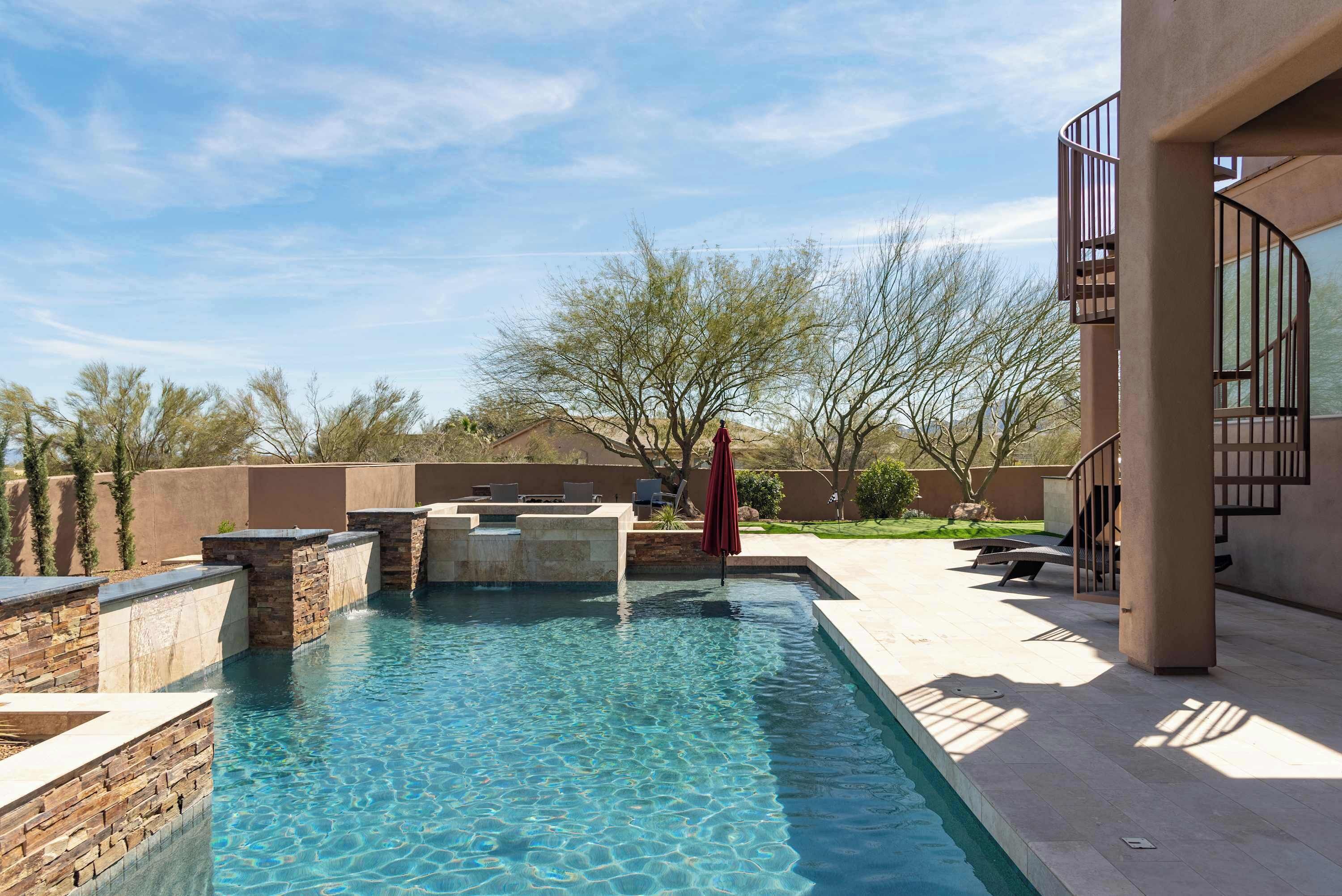A swimming pool with stone walls, a red umbrella, and a view of the surrounding landscape.