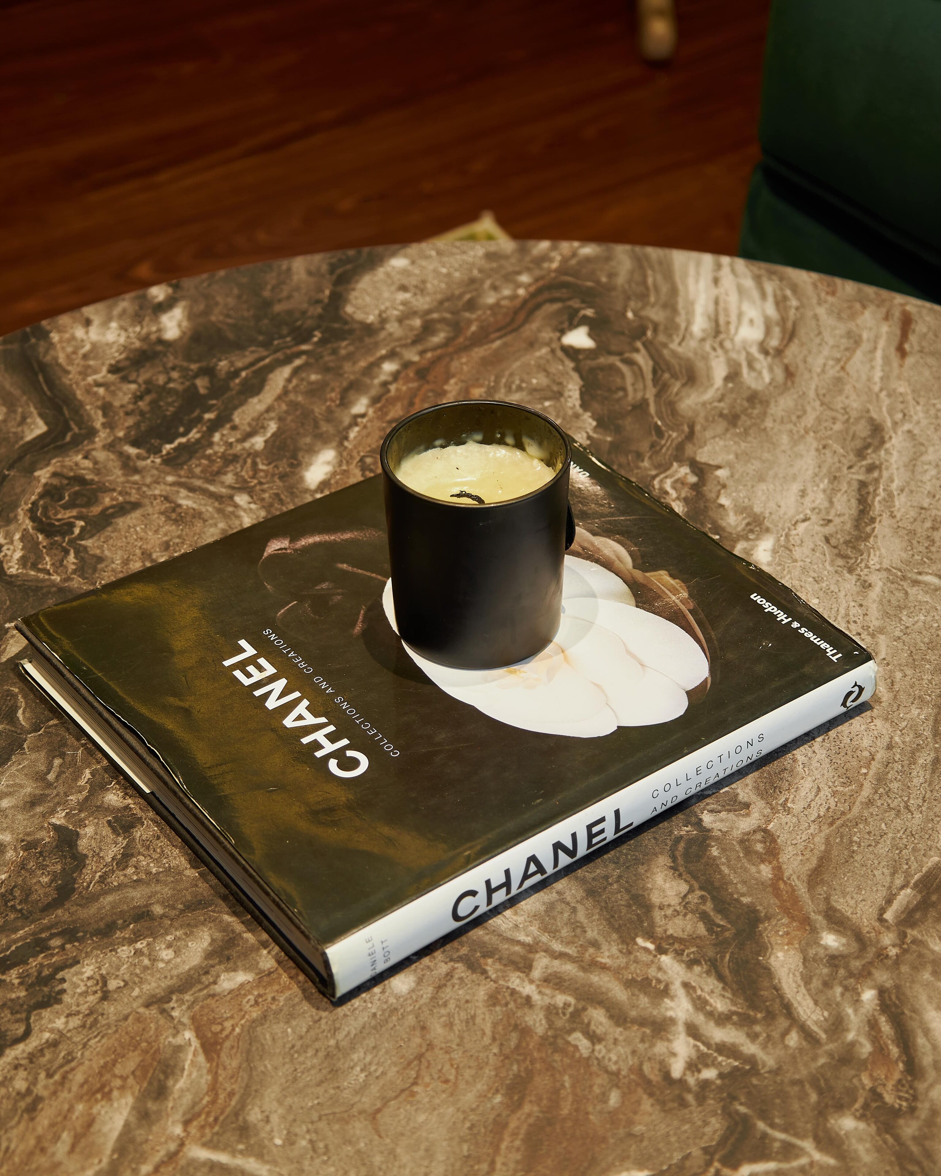 Ein Buch mit dem Titel 'CHANEL', aufgesetzt eine Kerze, platziert auf einem Marmortisch.