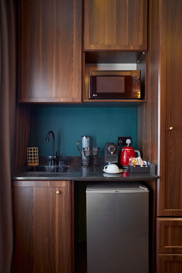 A compact kitchen with wooden cabinets, a microwave, a coffee maker, and a refrigerator. - The Hendon House (Lagos)