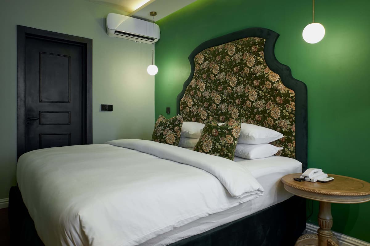 A neatly made bed with white linens, a floral headboard, a bedside table with a telephone, and an air conditioning unit on the wall.