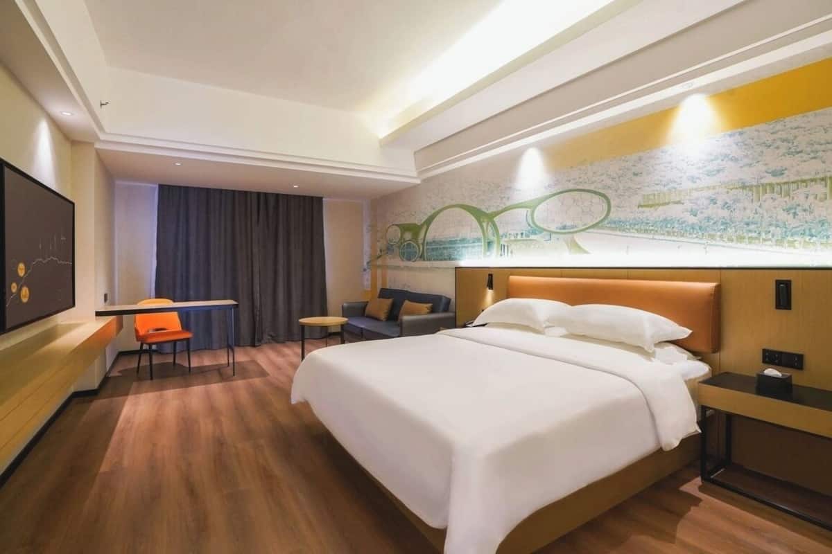 A hotel room with a large bed, a desk, a chair, and a television.
