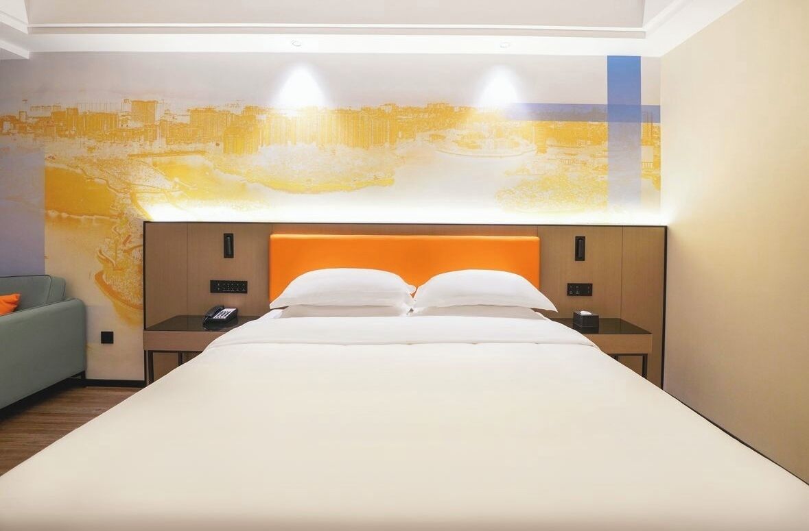 A modern hotel room with a large bed, a sofa, and a cityscape mural on the wall.