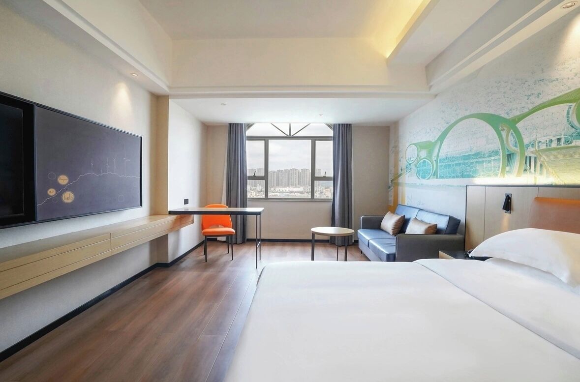 Een hotelkamer met een groot bed, een bureau, een stoel, een bank en een aan de muur bevestigde televisie.