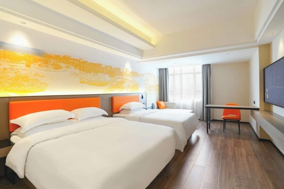 A hotel room with two beds, a desk, and a TV.