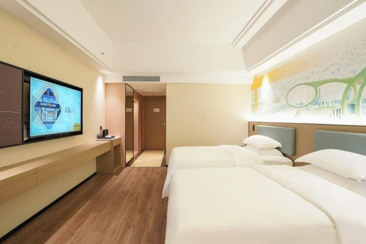 A hotel room with two beds, a TV on the wall, and a map on the wall.