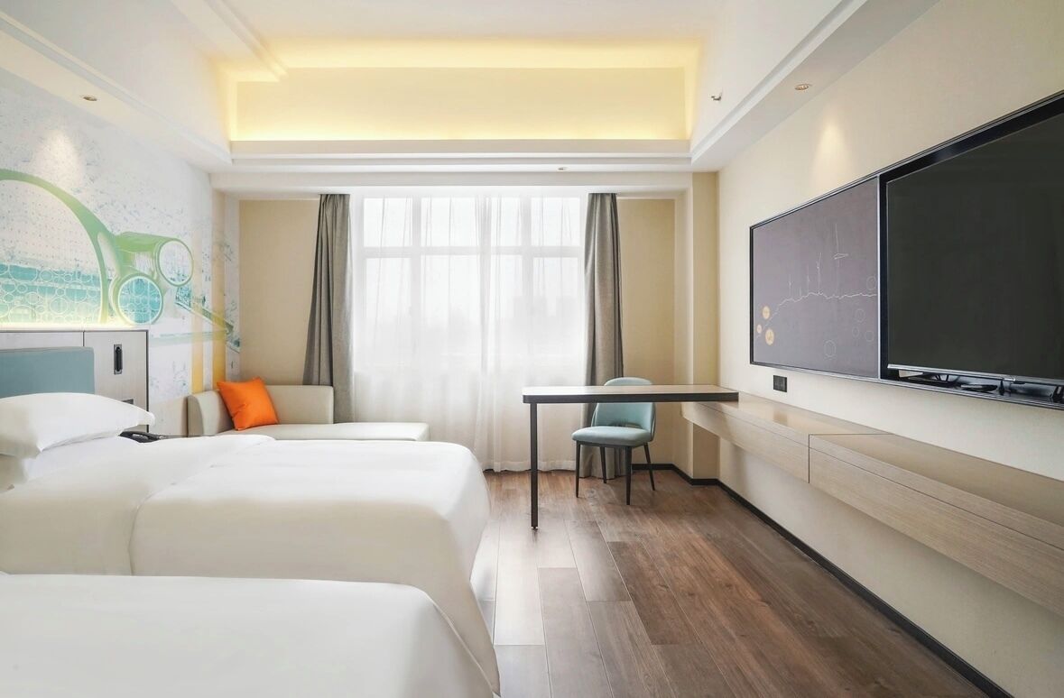 Una habitación de hotel con dos camas, un escritorio, un televisor y un ventanal con cortinas.